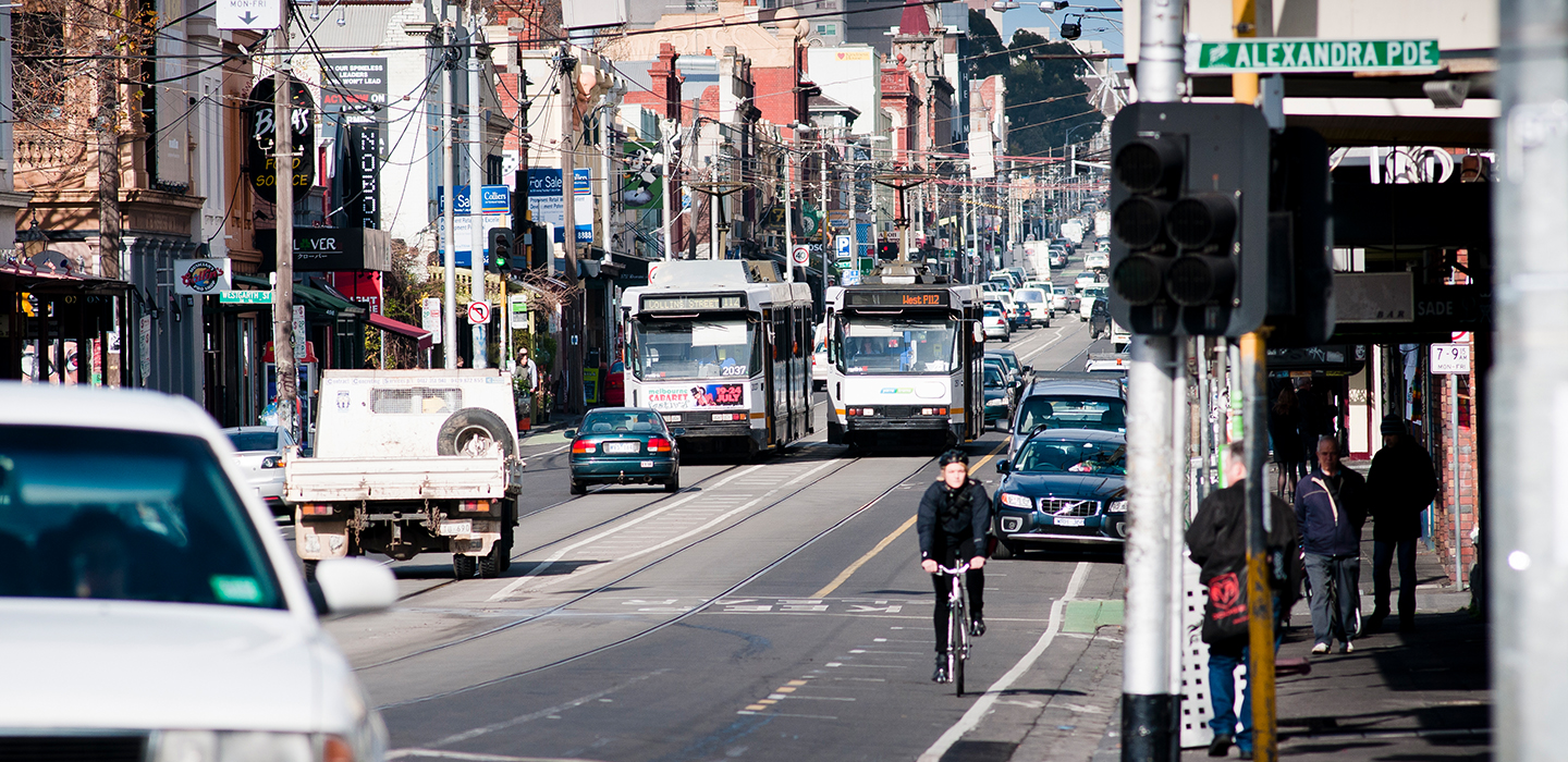 Lots of trams, cars and bike riders on a busy road